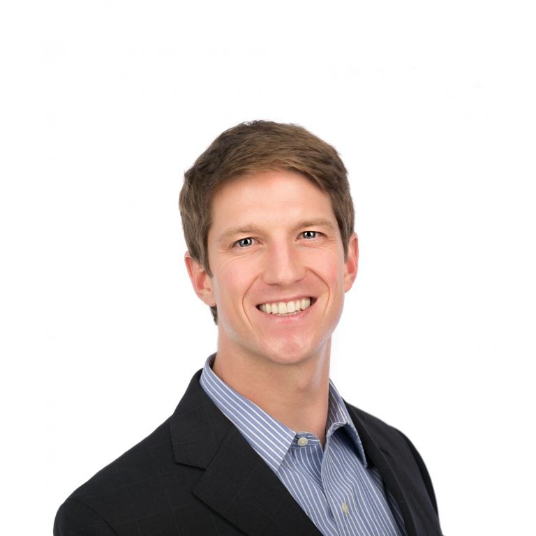 man in striped shirt and jacket smiles at the camera