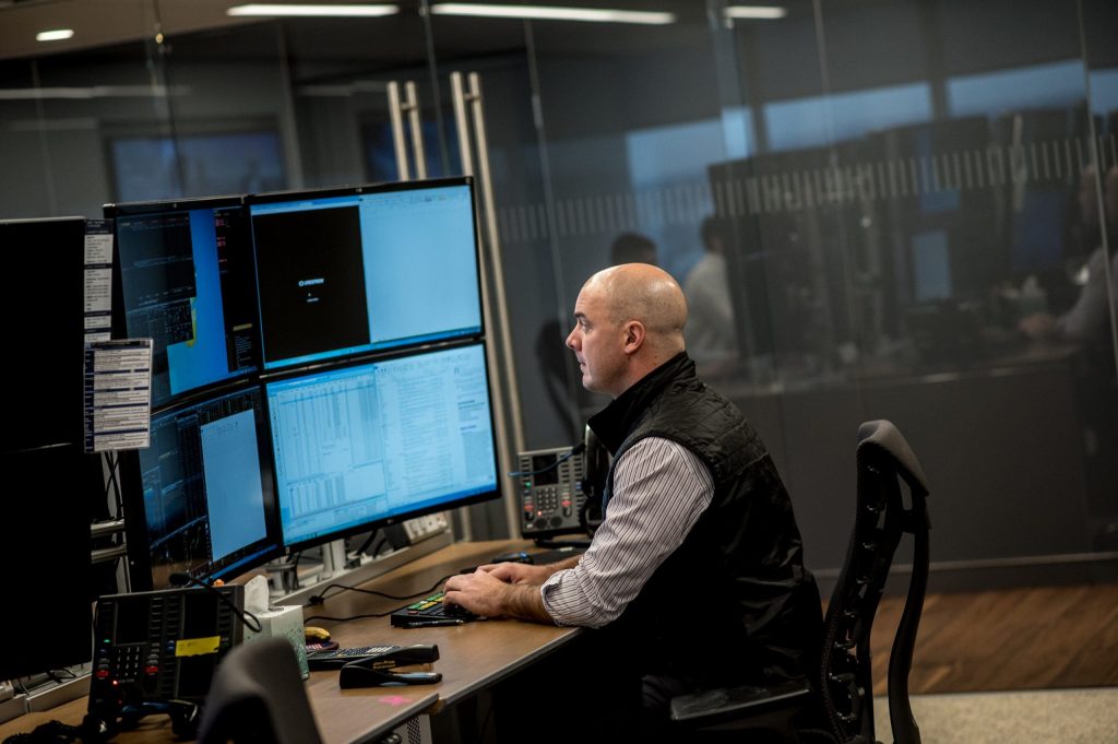 a man dressed in a black vest is sitting in front of a monitor programming
