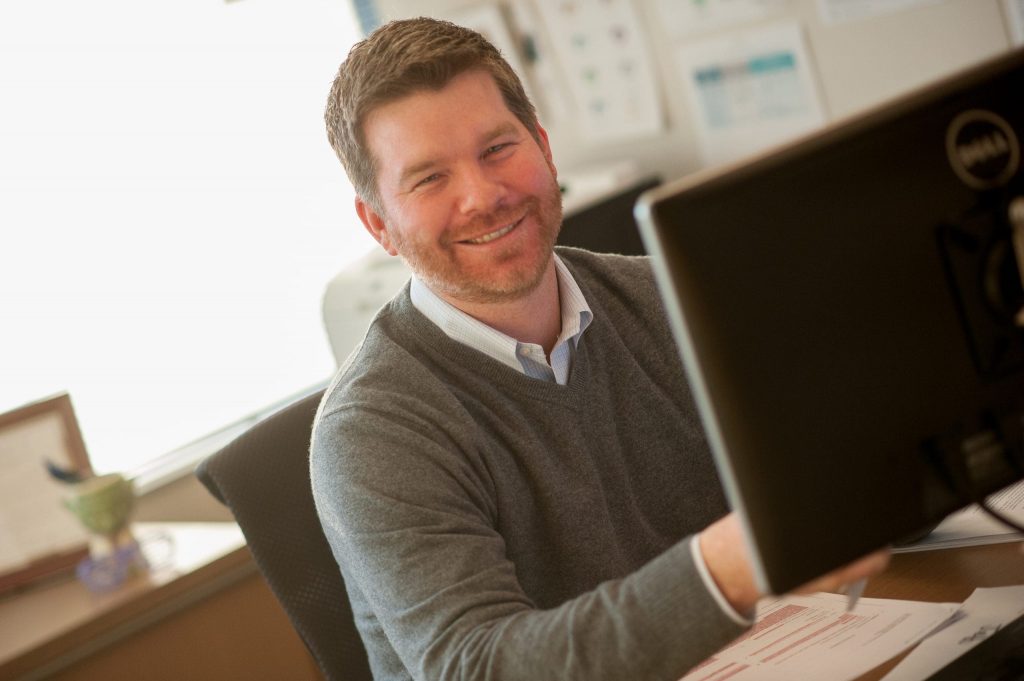 the man sitting in front of the computer smiles and looks at the camera