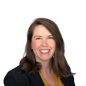 a woman with brown hair wearing a black jacket and a mustard dress smiles at the camera