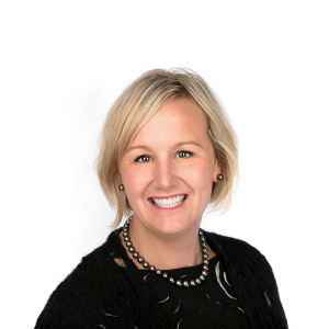 blonde haired woman in a necklace wearing a black blouse smiles at the camera