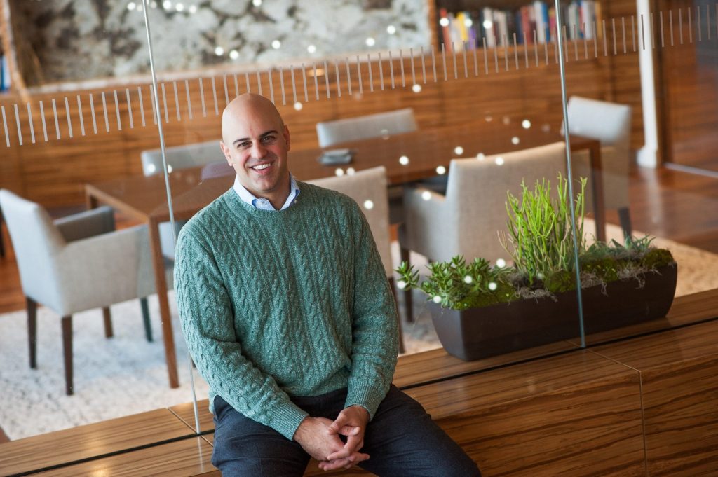 a bald man in a green sweater smiles at the camera