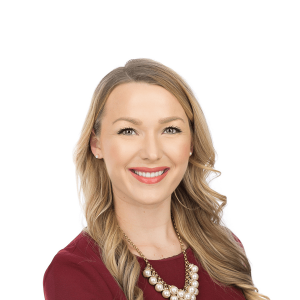 a woman with blonde hair in a gold necklace with pearls in a burgundy shirt smiling at the camera