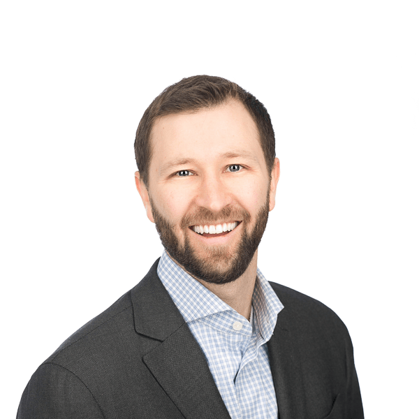 man in dark hair with a beard in a gray jacket and a light blue checkered shirt smiles at the camera