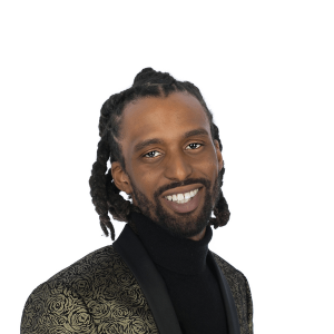 man in dreadlocks in a gold black jacket smiles at the camera