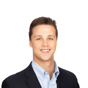 young man in light brown hair wearing a black jacket and a light blue shirt smiles at the camera