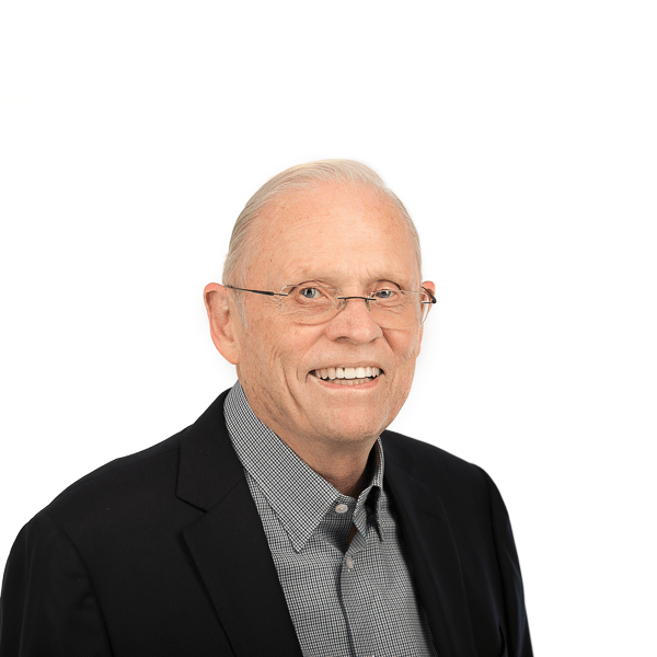 an elderly man with glasses wearing a gray patterned shirt with a black jacket smiles at the camera