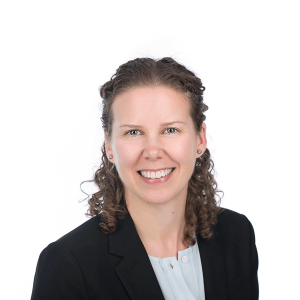 woman with curly brown hair wearing a black jacket and light blue shirt smiles at the camera