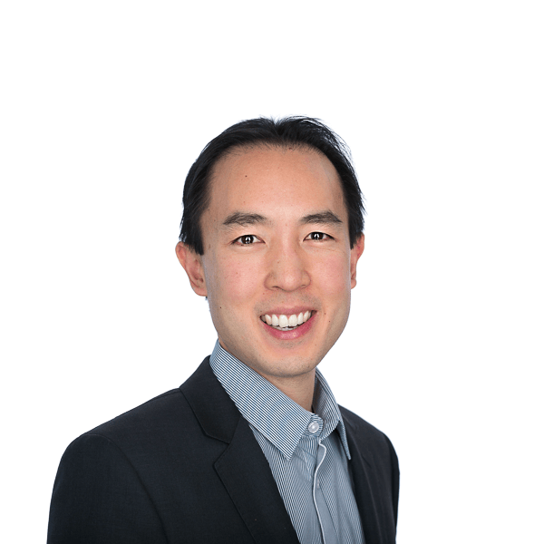 an asian man with black hair in a black jacket and bright blue shirt smiles at the camera