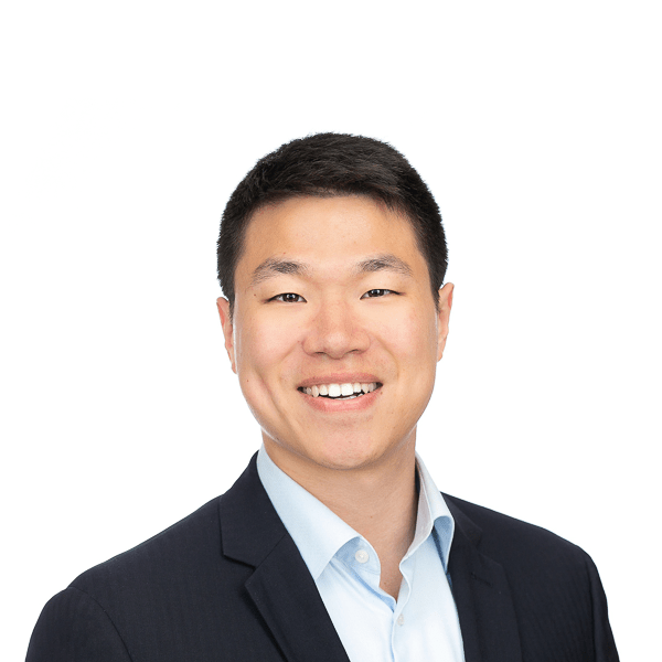 an asian man with black hair wearing a light blue shirt and black jacket smiles at the camera