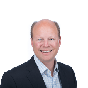 a bald man in a black jacket and a blue and white checkered shirt smiling at the camera