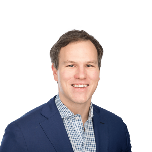 a man with brown hair in a navy blue jacket and a checked shirt smiles at the camera