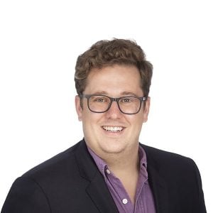 man in fair hair with glasses smiles at the camera