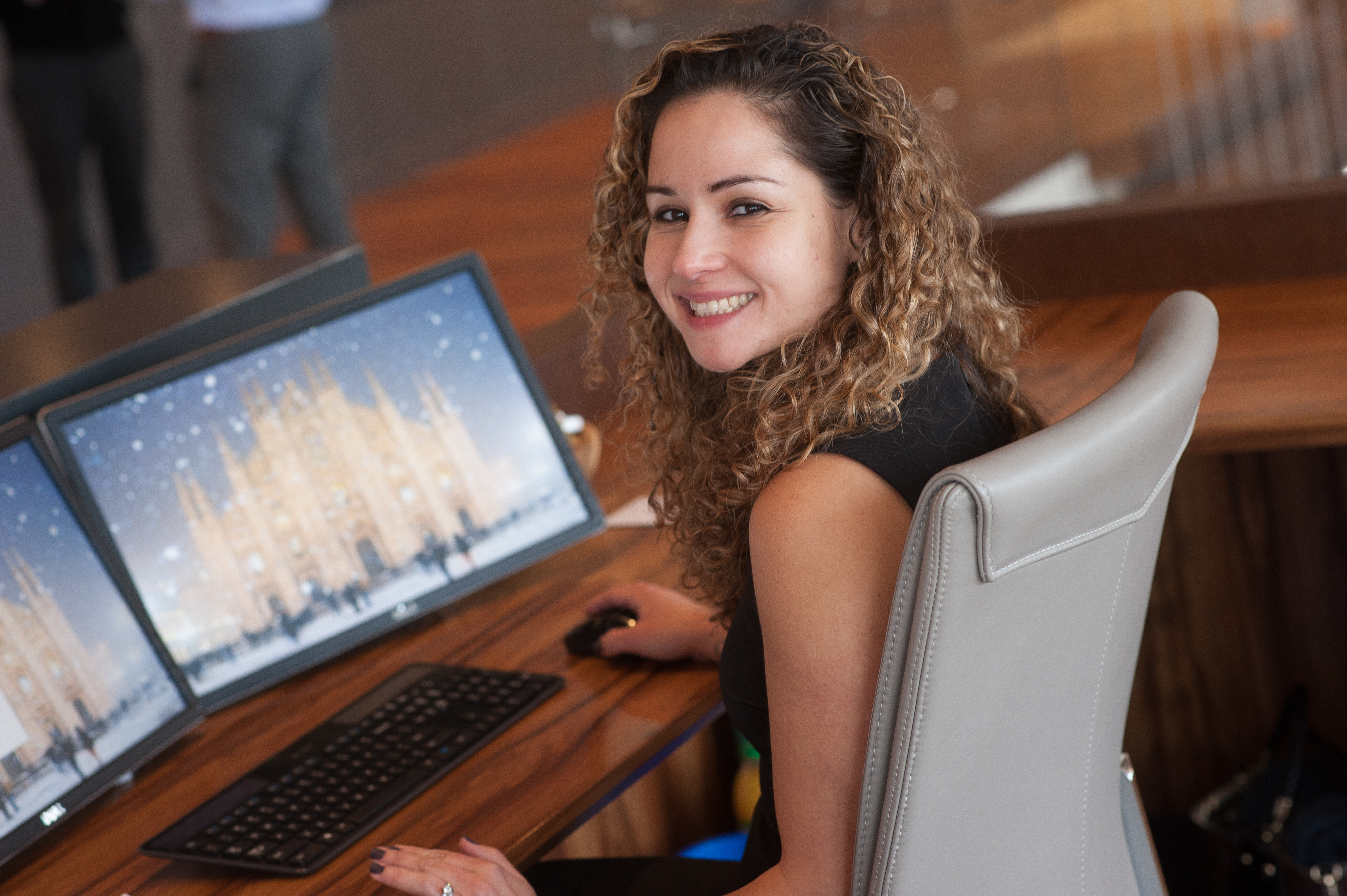 curly haired woman working in front of the computer smiling at the camera