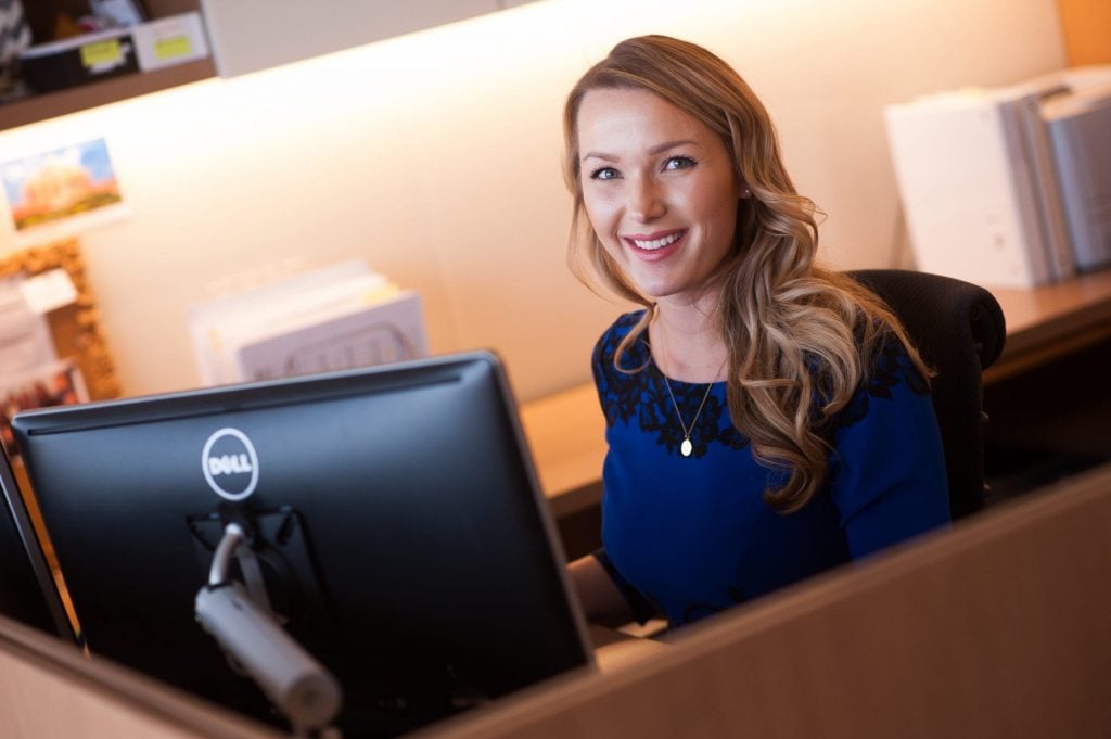 blonde woman working in front of computer smiling at camera