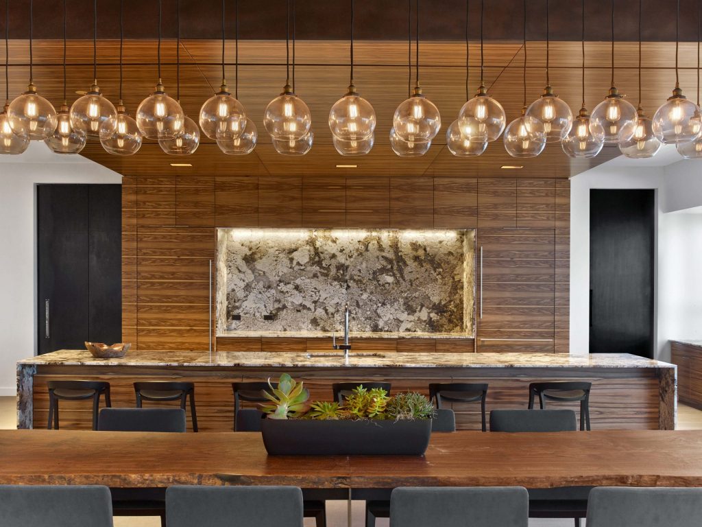 a row of lamps hanging over a marble top with chairs and a plant on the table