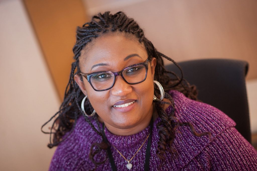 a woman with glasses and a burgundy sweater smiles at the camera