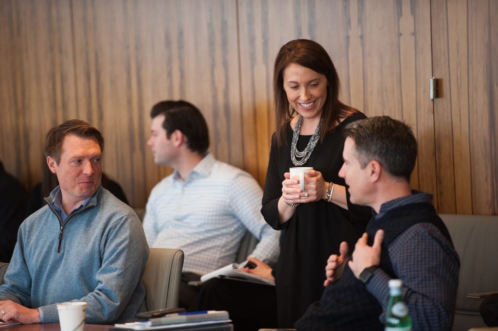 a woman in a black dress holding a cup is talking to the men