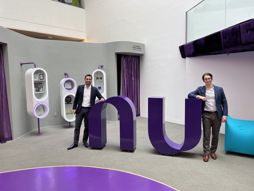 Two men lean against nu logo