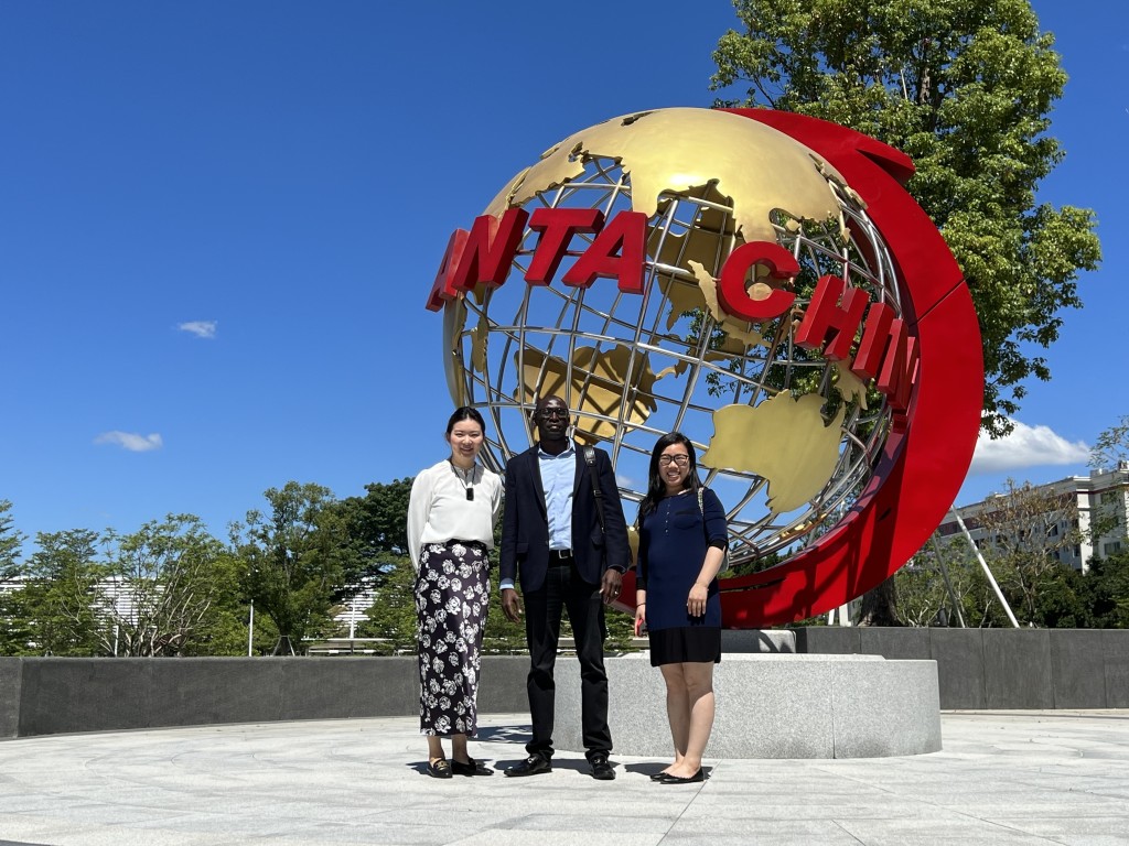 Three people in front of large globe with anta china logo